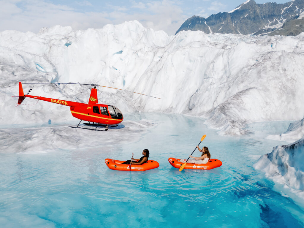 Elopement Couple kayaking in a glacier pool with helicopter
